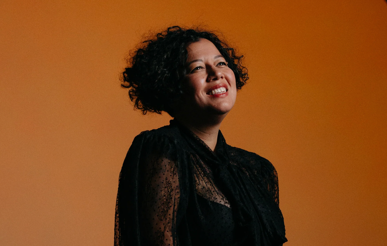 Portrait of Australian singer Mahalia Barnes smiling against a warm orange backdrop.